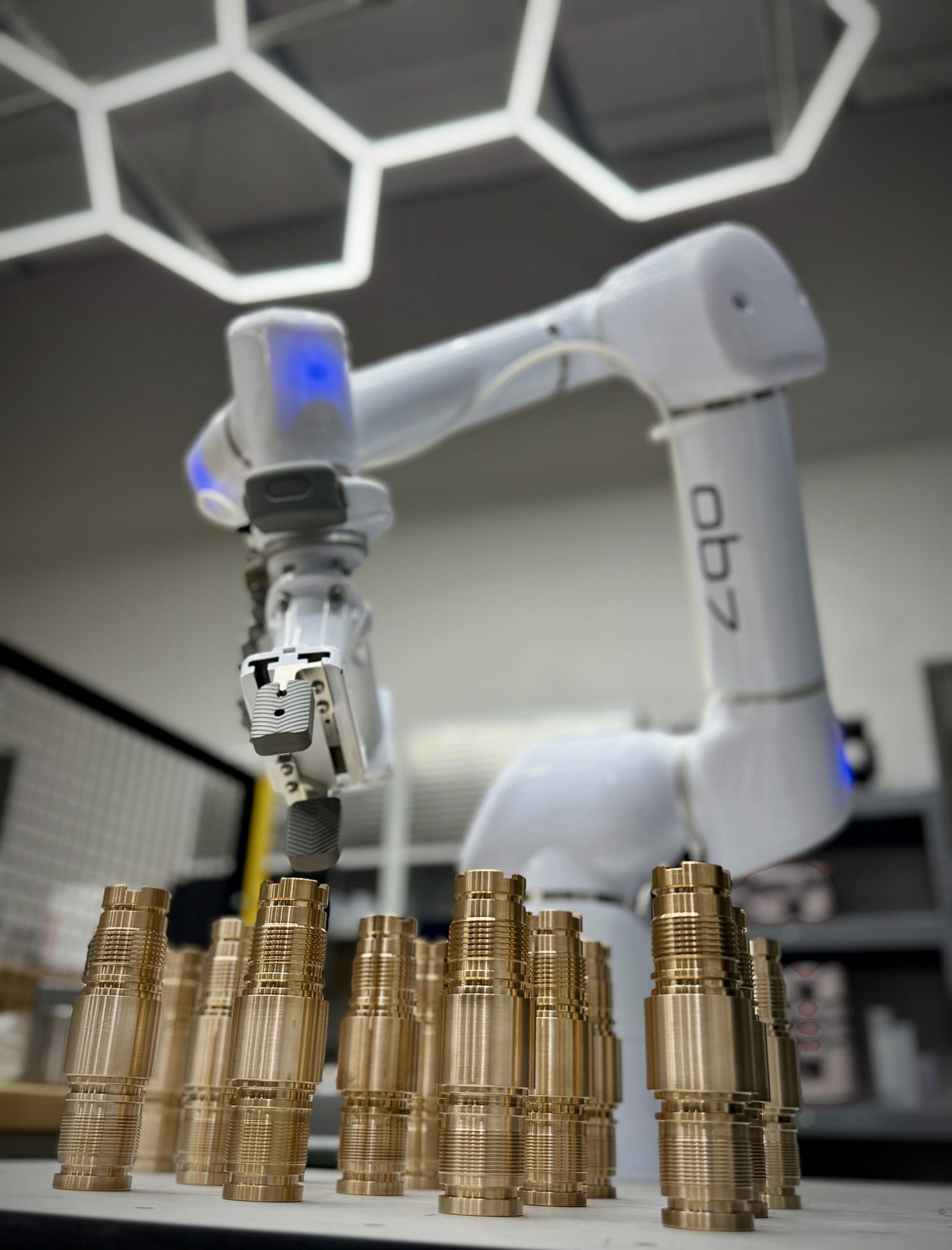 Collaborative robot arm above a batch of freshly machined copper-alloy components