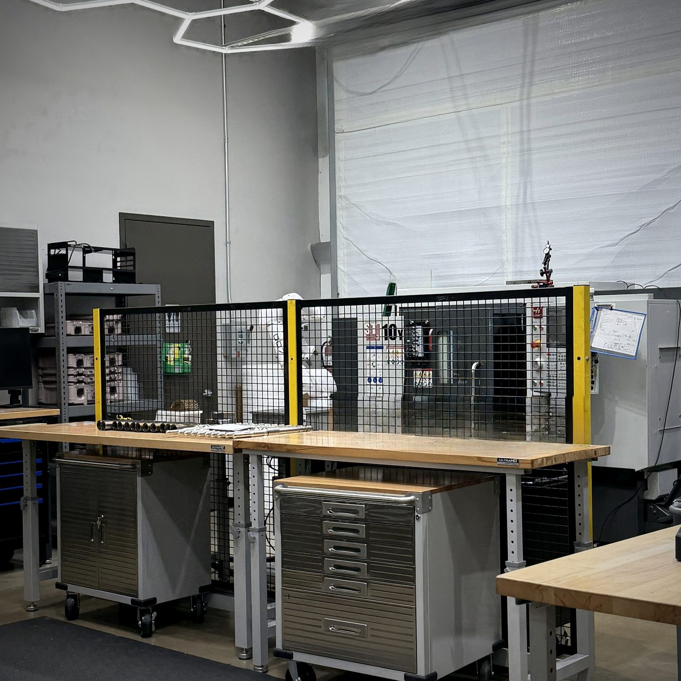 Assembly and staging bay under hexagonal LED lighting with a guarded robot cell behind